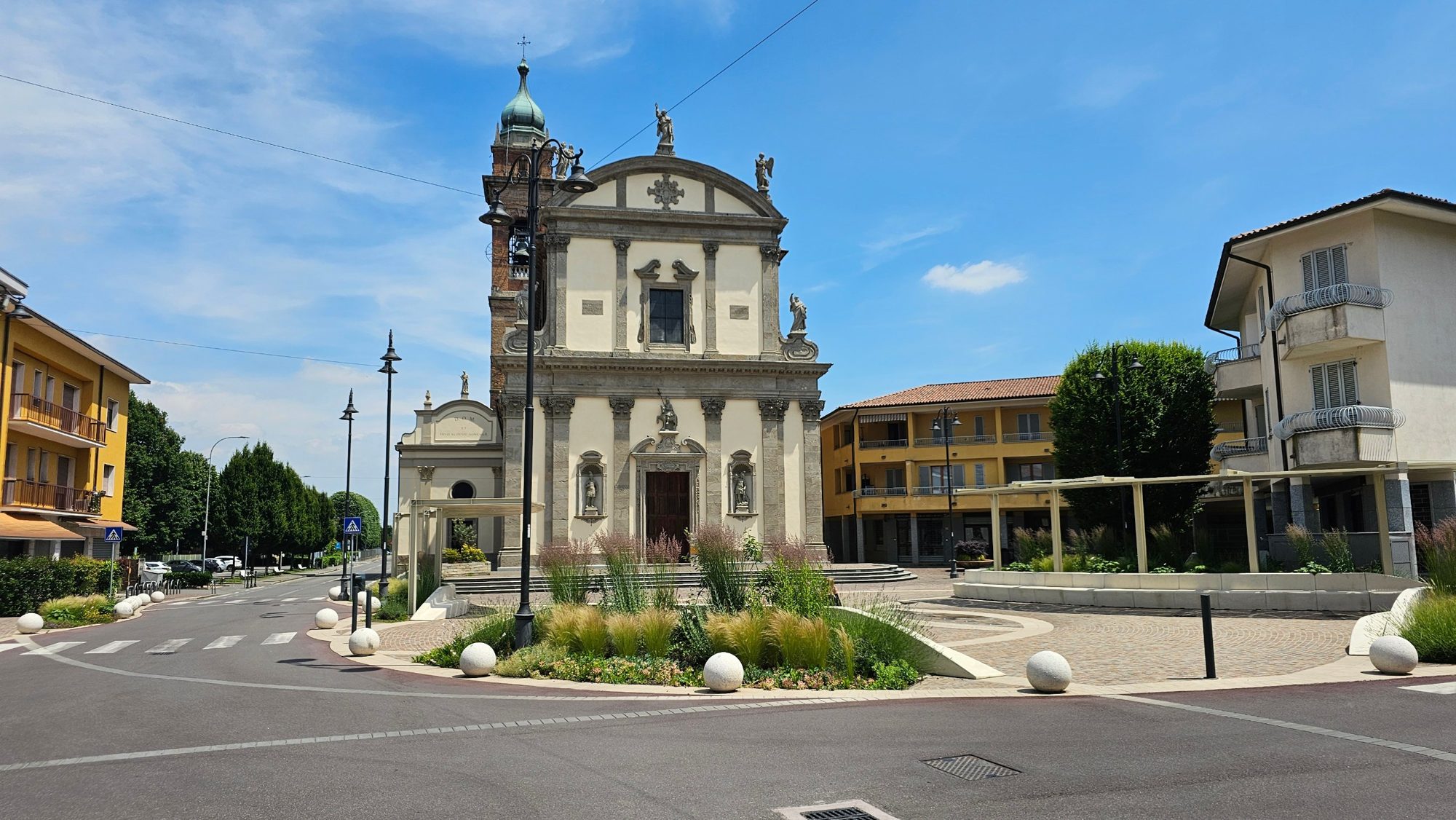 Piazza San Vittore di giorno, con la chiesa parrocchiale, le aiuole e i pergolati